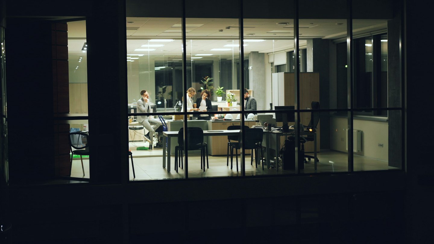 Quattro professionisti collaborano in un moderno ufficio di vetro di notte.